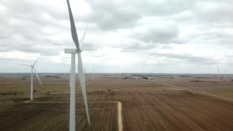 Lowering-aerial-view-of-a-farm-yard,-fields-and-wind-turbines-that-are-turned-off-on-a-cloudy-spring-day-in-south-central-Nebraska