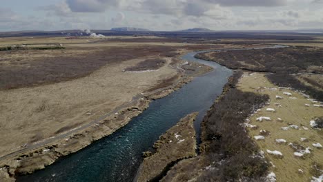 Aerial-flyover-tranquil-Bruara-River-surrounded-by-wide-rural-landscape-in-Iceland-during-cloudy-day