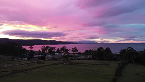 Stunning-purple-sunset-over-island-beach,-aerial-drone-pan-around-bay-with-epic-sky-and-mountain-range-with-small-shack-and-forest