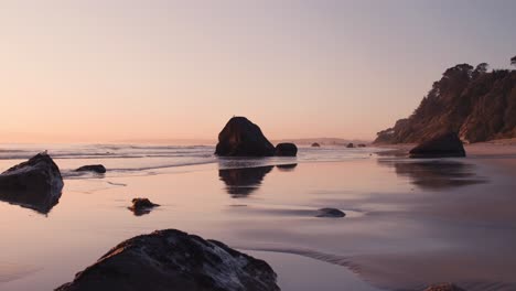 Rocks-scattered-on-smooth-luminous-beach-during-dreamy-morning-sunrise