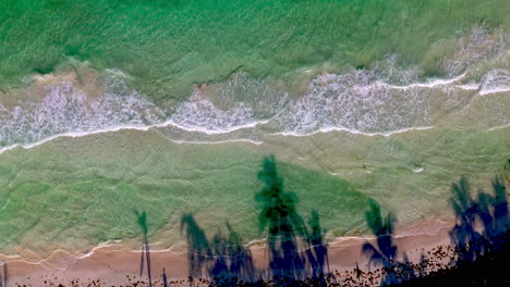 Downward-angle-drone-shot-rising-on-clear-ocean-waters-with-waves-crashing