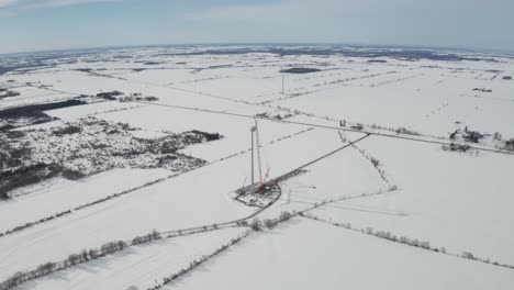 High-altitude-aerial-view-from-drone-backing-away-from-wind-energy-construction-site-in-winter-with-snow-covered-landscape