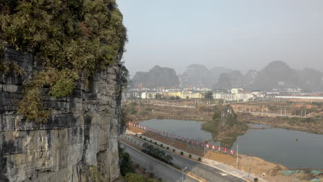 Action-shot-of-female-rock-climber-on-mountain-rock-face,-Chinese-city-backdrop