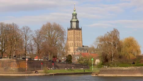 Flauschige-Wolken-Ziehen-über-Den-Turm-Der-Kathedrale-Walburgiskerk,-Gesehen-Von-Der-Anderen-Seite-Der-Ijssel,-Vorbei-Am-Stadtbildkai-Der-Mittelalterlichen-Stadt-Zutphen-In-Den-Niederlanden