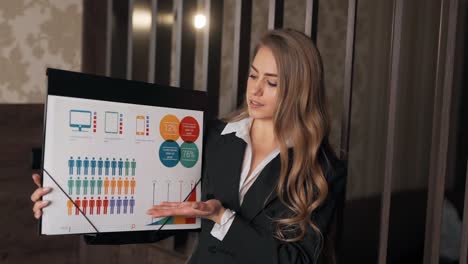Nice-adult-girl-in-a-business-suit-shows-a-presentation-on-infographics-looking-at-the-camera