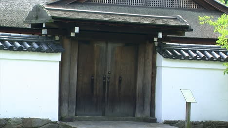 Close-up-of-the-roofed-hinoki-wood-entrance-gate-and-tiled-wall-of-a-Japanese-house
