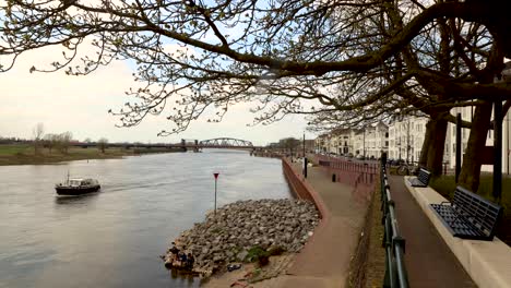 Urban-countenance-landscape-time-lapse-with-people-strolling-by-and-relaxing-along-the-river-IJssel-embankment-of-Hanseatic-Dutch-city-Zutphen-with-water-and-recreational-boats-passing-by