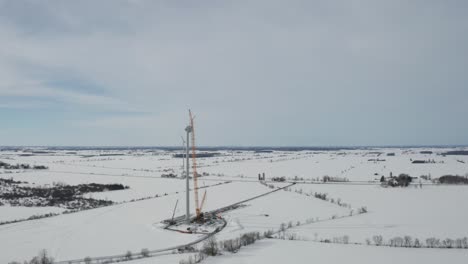 Stunning-winter-aerial-view-of-wind-power-construction-site-covered-in-show-with-crane-against-tower