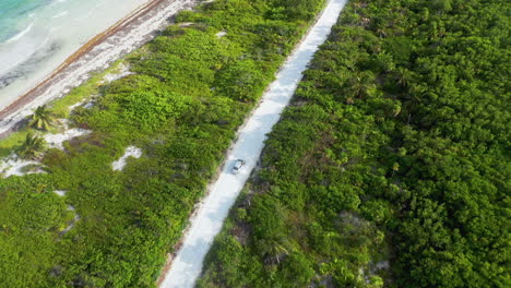 Filmische-Drohnenaufnahme-Eines-Autos,-Das-Entlang-Der-Natürlichen-Küste-In-Der-Nähe-Von-Mahahual-Mexiko-Mit-Dichtem-Wald-Und-Klarem-Ozeanwasser-Fährt