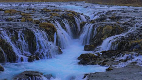Breiter-Schuss-Von-Isländisch-Blauem-Wasser-Von-Brückenfällen,-Die-Abends-Die-überwucherten-Felsen-Hinunterfallen