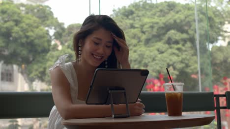 Schöne-Junge-Charmante-Asiatin,-Die-Internetanruf-Auf-Ihrem-Tablet-Hat-Und-Im-Café-Lächelt