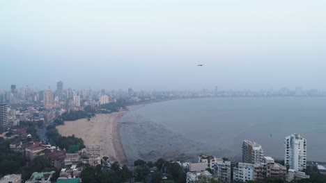 A-cinematic-drone-shot-of-the-famous-Marine-Drive-Chaupati-Beach-point-in-South-Bombay-region-of-Mumbai-City,-overlooking-the-hanging-garden-hill-and-forest-in-a-slow-smooth-motion