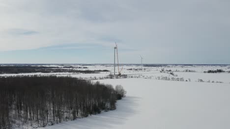 Drone-flying-over-snow-covered-farm-fields-with-wind-farm-and-windmills-on-horizon
