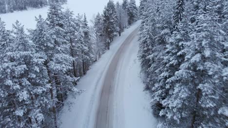 Northern-snowy-mountain-road-through-alpine-forest---Aerial-fly-over