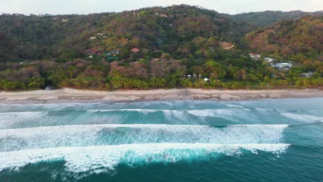 Aerial-above-turquoise-water-with-huge-waves,-beach,-coastline-and-surfers-in-the-pacific-ocean-in-Tamarindo,-Costa-Rica