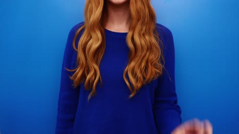 Young-redhead-woman-in-blue-shirt-showing-peace-gesture,-isolated-on-the-blue-background