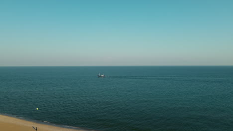 Aerial-wide-shot-of-boat-cruising-on-blue-Baltic-Sea-and-people-flying-kite-on-golden-beach-of-Hel,Poland