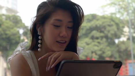 Porträt-Eines-Schönen-Jungen-Charmanten-Asiatischen-Mädchens,-Das-Internetanruf-Auf-Ihrem-Tablet-Hat-Und-Im-Café-Lächelt