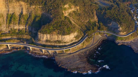 Bird's-Eye-View-Of-Sea-Cliff-Bridge-With-Lawrence-Hargrave-Drive-At-Sunrise-In-Clifton,-Australia