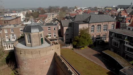 Sideways-pan-around-top-of-historic-Bourgonje-stronghold-tower-and-city-wall-in-Zutphen,-The-Netherlands,-with-grass-vegetation-roof-on-the-other-side-and-tree-branches-entering-the-foreground