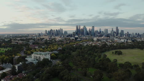 Cityscape-of-Melbourne-with-gorgeous-colourful-sky-revealing-park-below,-aerial-jib-shot