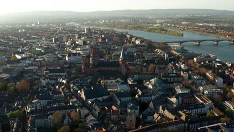 full-drone-shot-of-the-red-Cathedral-church-of-Mainz-in-the-middle-of-the-old-town-and-tiny-houses-with-the-Rhine-river-in-the-back-in-Germany