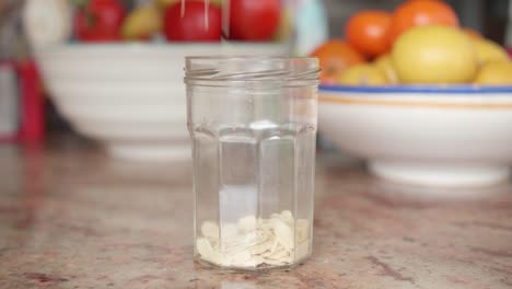 Bulk-sliced-or-flaked-organic-almonds-being-poured-in-a-glass-jar-on-a-kitchen-table