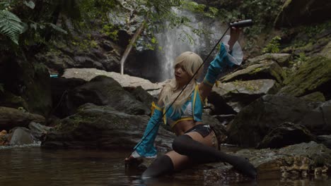 Lucy-heartfilia-cosplayer-holds-her-rope-in-position-as-she-sits-at-the-base-of-a-waterfall