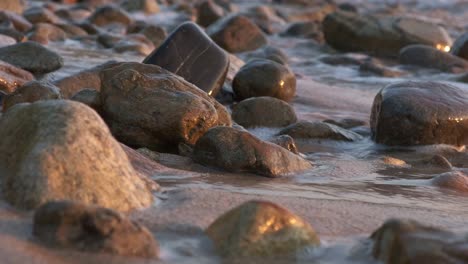waves-lap-on-a-rocky-beach-with-soft-warm-light-with-smooth-pebble-like-rocks