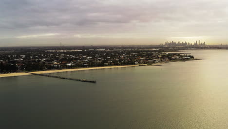 Beautiful-aerial-parallax-of-cityscape-rotating-around-long-wooden-pier-during-the-morning's-golden-light