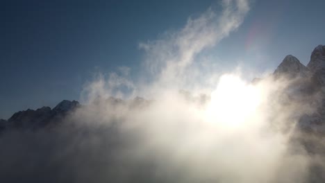 Drohnenflug-Durch-Wolken-Gegen-Sonne-Und-Berge,-Alpen,-Vrsic-Pass,-Slowenien
