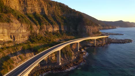 Curvy-Sea-Cliff-Bridge-Road,-A-View-Of-Majestic-Mountains-And-Clear-Blue-Waters-Of-Tasman-Sea-In-NSW-Australia---aerial-shot