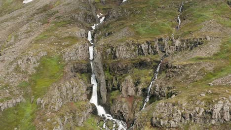 Powerful-flow-of-water-on-steep-rocky-cliff-of-Iceland-mountain,-aerial