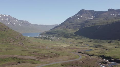 Aerial-above-mossy-valley-with-mountains-and-distant-Seyðisfjörður-town