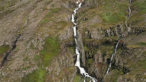 Cascada-De-Agua-Derretida-En-La-Ladera-Rocosa-De-La-Remota-Montaña-De-Islandia,-Antena