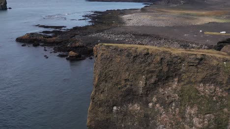 Flying-past-steep-cliffs-revealing-large-boulders-on-beach-in-Iceland