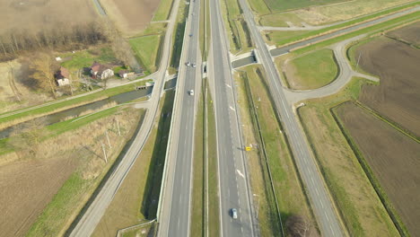 Aerial-flyover-driving-highway-surrounded-by-agricultural-fields-during-sunlight