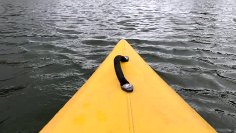 The-yellow-color-nose-of-kayak-moving-along-calm-river-or-lake-on-a-nice-sunny-day,-outdoor-activities
