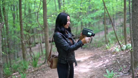 Young-attractive-woman-captivated-by-an-old-fashion-film-camera-in-the-woods-during-the-day---concept:-memories,-old,-retro,-hobby,-tourist,-trying-new-things---medium-gimbal-shot-in-slow-motion