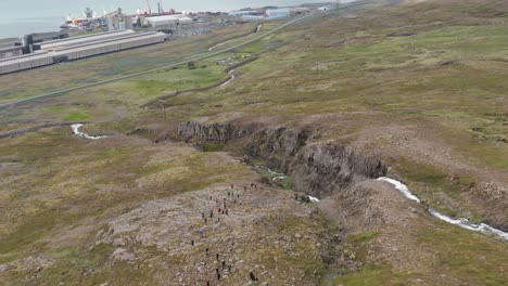 Aerial-of-hiking-group-going-up-mountain-with-Alcoa-Fjarðaál-industrial-area-in-background