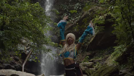 Erstaunliches-Fitness-Mädchen-In-Einem-Anime-Cosplay-Kostüm,-Das-Die-Natur-Am-Fuße-Eines-Epischen-Wasserfalls-Genießt