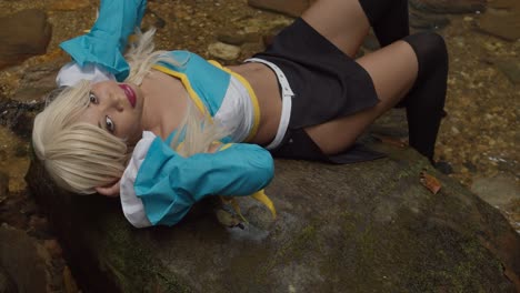 Crystal-clear-waters-flowing-from-a-waterfall-while-an-anime-cosplayer-lays-on-the-rocks-and-smile