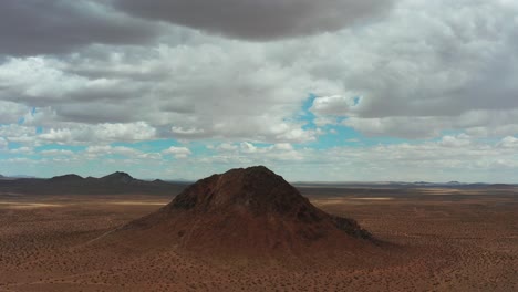 Ein-Kegelförmiger-Berg-Thront-An-Einem-Bewölkten-Tag-über-Der-Mojave-Wüstenlandschaft---Umlaufende-Luftaufnahme