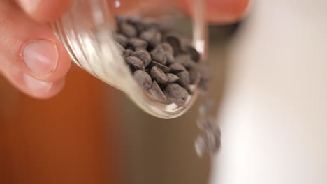 Pouring-Chocolate-Chips-from-Plastic-Cup,-Close-Up-in-Slow-Motion-with-Copy-Space