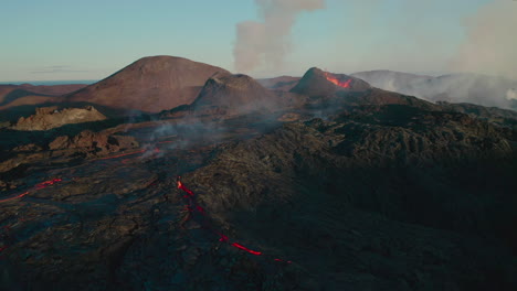 Aerial-flyover-epic-volcanic-area-with-erupting-volcano-crater-and-flowing-lava-during-blue-sky-and-sunlight-in-Iceland