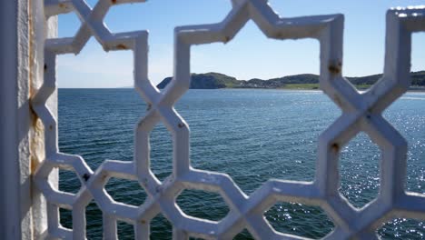 North-Wales-green-mountain-island-coastline-through-ornate-patterned-wrought-iron-railing-jib-up-left