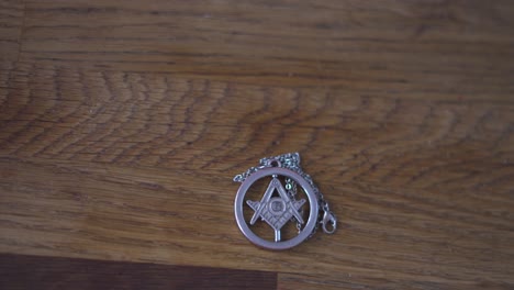 A-pan-over-in-different-speeds-of-Masonic-Freemason-talisman-necklace-with-G-symbol-sitting-on-wood-table-in-4K-60fps