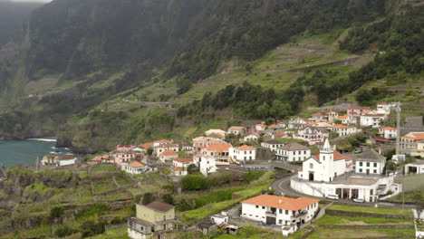 Circling-drone-aerial-footage-of-Sexial-town-on-the-North-Coast-of-Madeira-island,-Portugal-with-mountain-backdrop