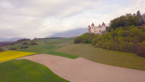 Cultivated-fields-around-Champvent-castle,-Switzerland.-Aerial-rising