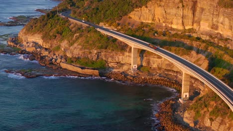 Vehicles-Travelling-At-Sea-Cliff-Bridge-Over-Calm-Blue-Ocean-At-Sunrise-In-New-South-Wales,-Australia
